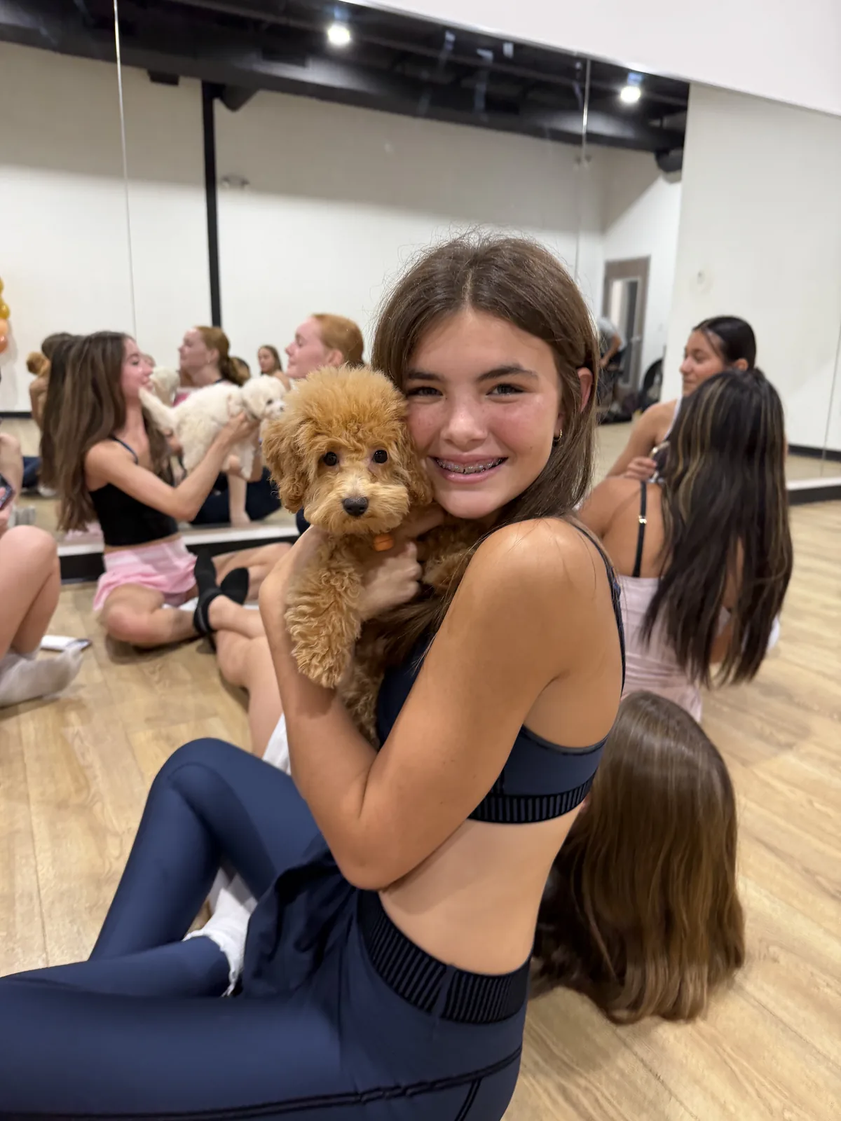 A teen smiling while holding an apricot puppy at a Pawty Yoga cuddle session