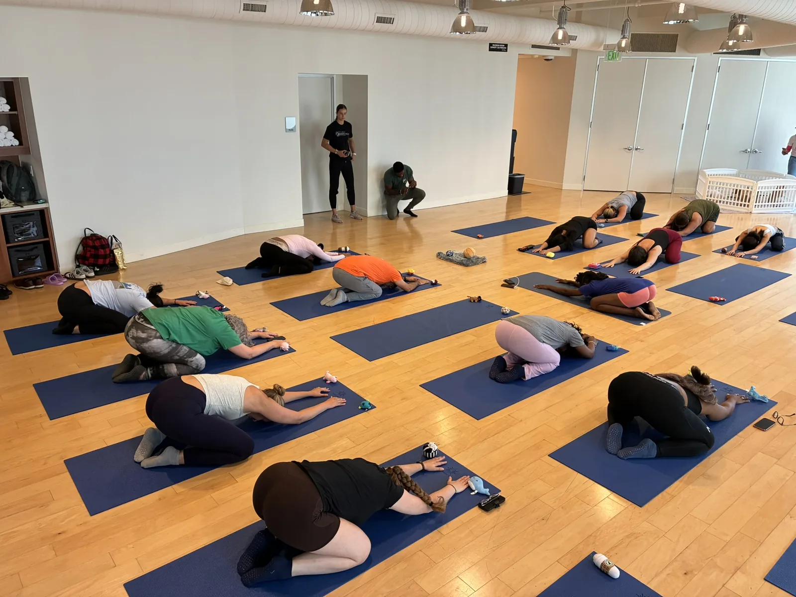 Adults resting in child's pose while puppies wander the mats at a Houston session