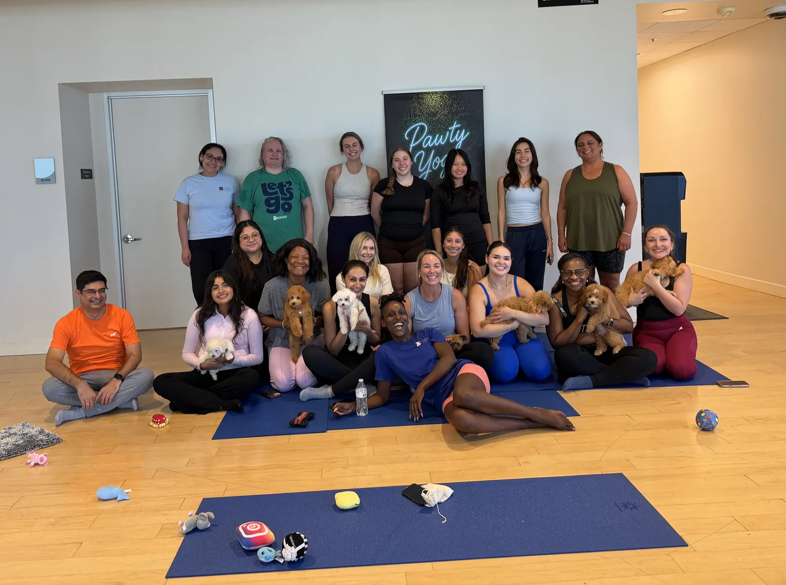 An adult group with puppies in a bright Houston studio during a Pawty Yoga therapy session