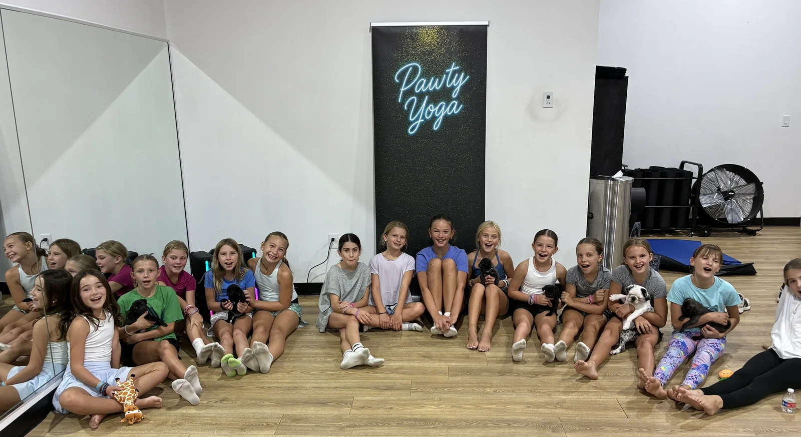 A full kids class with puppies and the Pawty Yoga banner at a Houston school-style event