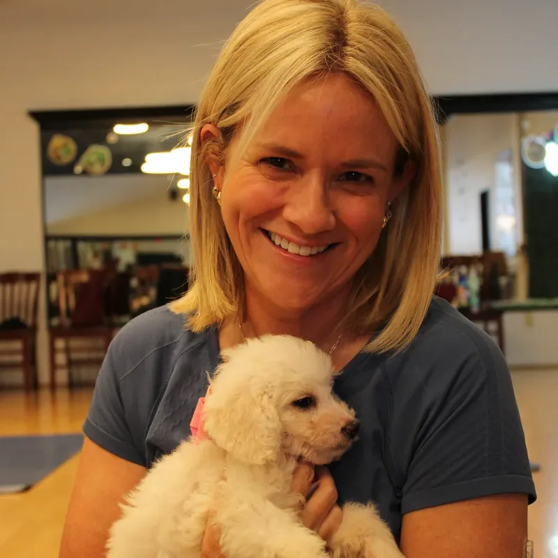 A smiling woman hugging a cream puppy at a Houston puppy yoga class