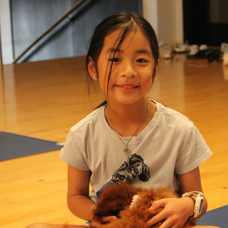 A young girl beaming with a puppy in her lap at Houston puppy yoga