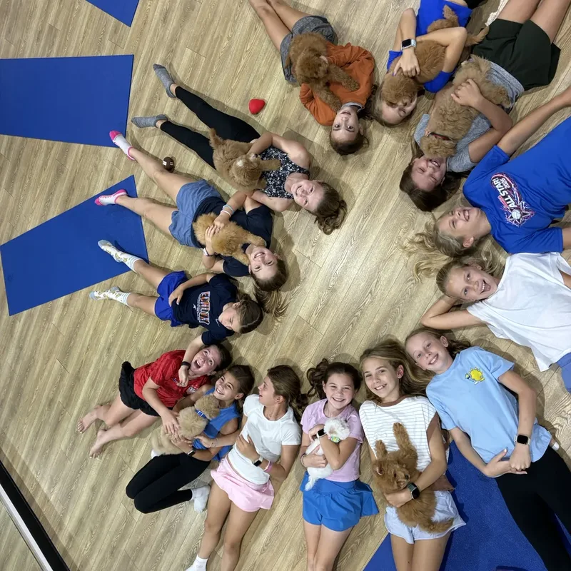 A circle of kids lying on the floor with puppies at a Houston puppy party