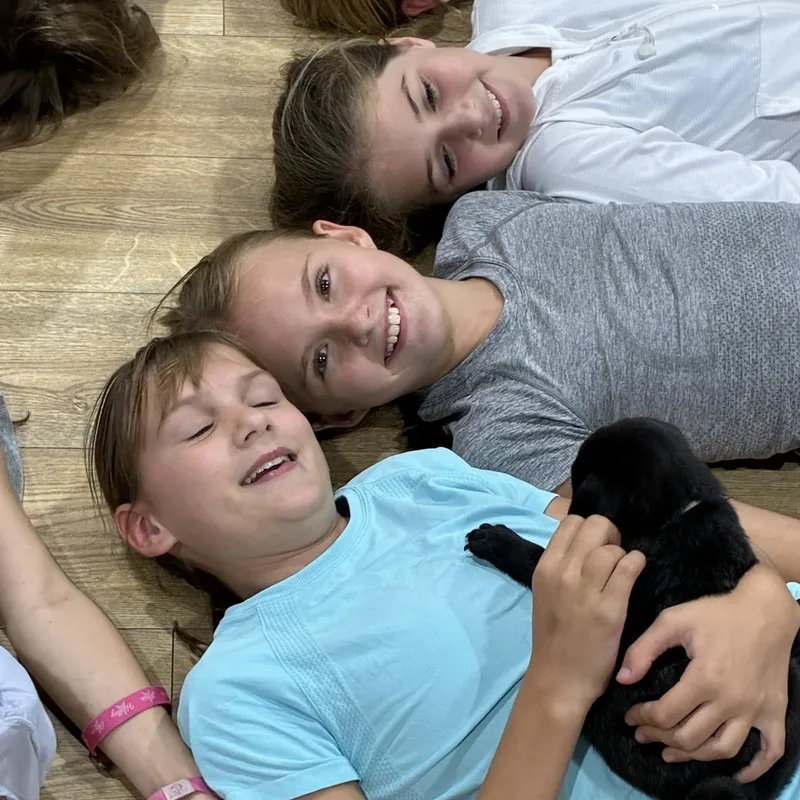 Two kids laughing while holding a black puppy at a Houston puppy yoga class