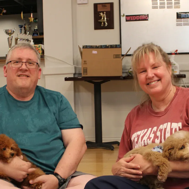 Grandparents smiling with puppies in their laps at a Houston holiday puppy yoga party