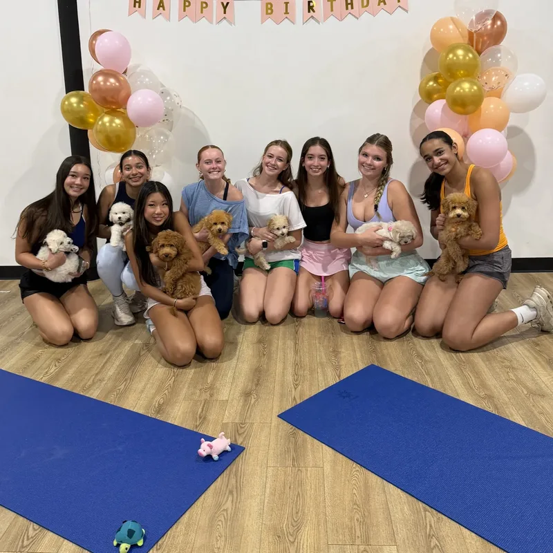 A group of girls holding puppies under a Happy Birthday banner at a Houston puppy party