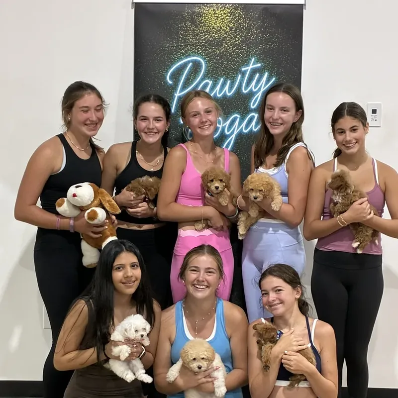 A group of friends holding puppies under the Pawty Yoga neon sign in Houston