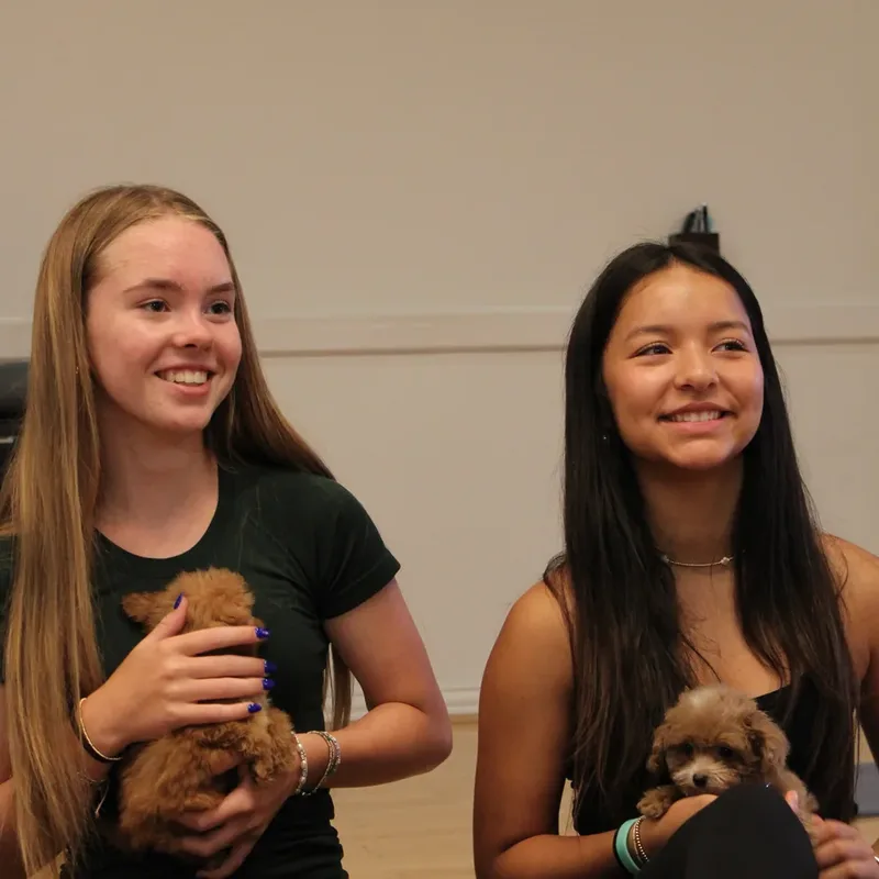 Two girls smiling with puppies at a Houston puppy yoga class