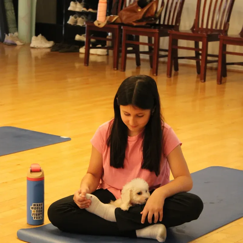 A girl sitting cross-legged on her mat with a puppy at Houston puppy yoga