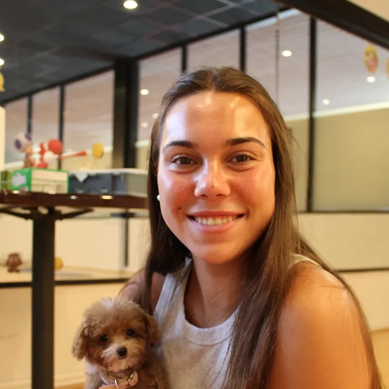 A smiling young woman holding a poodle puppy at Houston puppy yoga